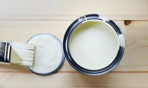 An open can of white paint with a paint brush resting on the lid next to it.