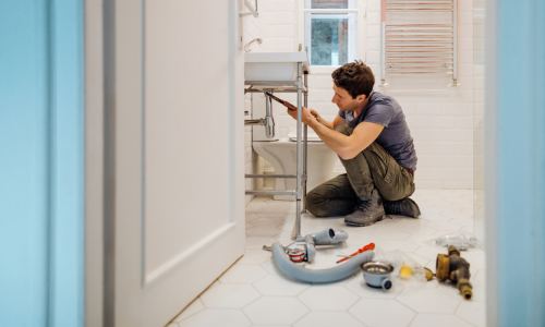 A contractor installing a pipe underneath a bathroom sink.